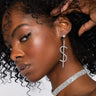 A person with curly hair showcases a sparkly, MO MONEY DOLLAR SIGN DANGLE EARRING from Y&S Davidson Inc and a shimmering choker necklace. The person's hand is raised to highlight the earring, and they have a smooth, glowing complexion.