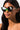 A person with long, dark hair is confidently sporting NO BULLSHIT CAT EYE SUNNIES featuring black lenses and green accents against a plain white background.