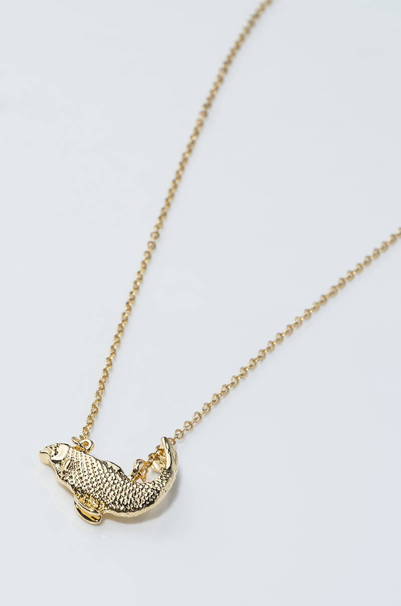 The PISCES FIGURE NECKLACE by YIWU MASTER boasts a delicate gold chain adorned with an intricately detailed, mermaid-shaped pendant. The mermaid appears to be laying down, bringing a whimsical touch to this elegant accessory. The necklace is showcased against a plain, light surface background.