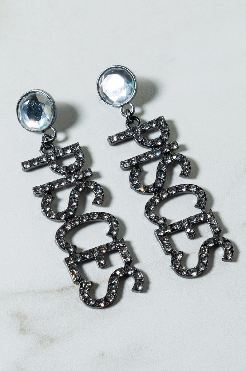 Introducing the PISCES RHINESTONE EARRINGS: a pair of sparkling earrings that feature "Pisces" written in block letters adorned with rhinestones. The round, gem-like studs add an extra touch of glamour, all beautifully displayed against a light, neutral background.