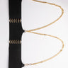 Introducing the PLUS ITS THE CHAINS FOR ME STRETCH HARNESS BELT, a stylish black belt adorned with gold-tone hardware and chain detailing. This elegant accessory features a series of gold eyelets and is connected by two gold chains that loop from the top to the bottom, adding a touch of sophistication to its sleek black design.