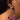 Close-up of a person wearing the POURING DANGLE EARRING by Mika Accessories. The gold earring has a circular cluster design adorned with sparkling gemstones in pink, green, and clear. The person has dark hair and a medium skin tone.