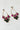 A delicate pair of POURING DANGLE EARRINGS by Mika Accessories features clusters of sparkling gemstones. The clusters include vibrant magenta, clear, and deep green stones arranged in a floral pattern, adding a touch of elegance and color contrast. These earrings cast a light shadow on the surface.