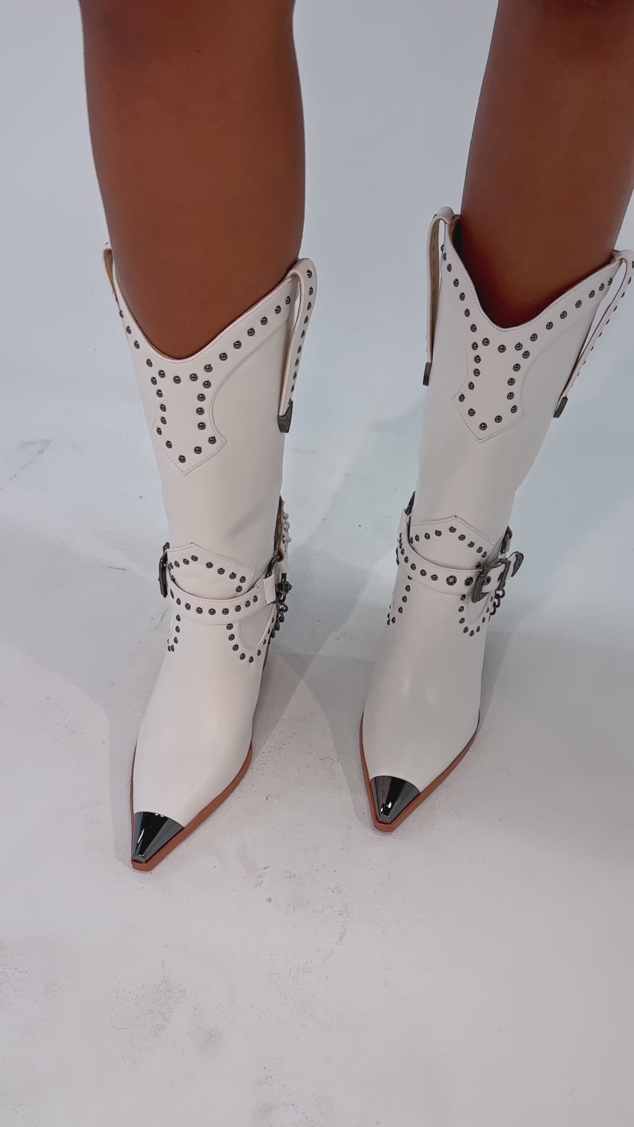 A video of a person wearing the AZALEA WANG OSBORN WHITE WESTERN BOOTIE, featuring silver studs, metal toe caps, and decorative buckles.