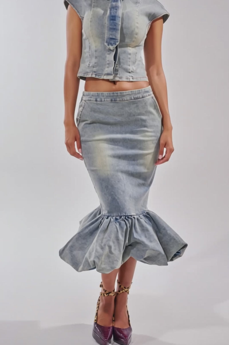 A video of a woman in the fitted, short-sleeve JOSIE DENIM BLOUSE with ruffle detail and a matching high-waisted mermaid skirt, styled with ankle-strap heels.