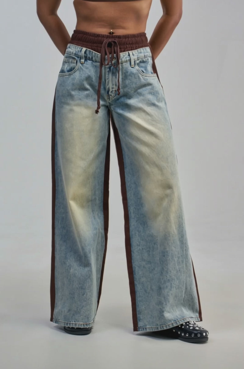 Video of a woman modeling the COOL LIKE ME DENIM JOGGER—wide-leg, light wash denim jeans featuring brown side stripes and an elastic waistband.