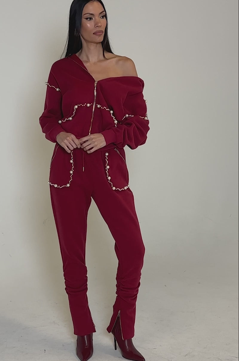 Video of woman modeling the COZY HOLIDAY PEARL SWEATSHIRT IN BURGUNDY, an oversized hoodie with pearl-like beads, and matching joggers, standing against a plain gray background