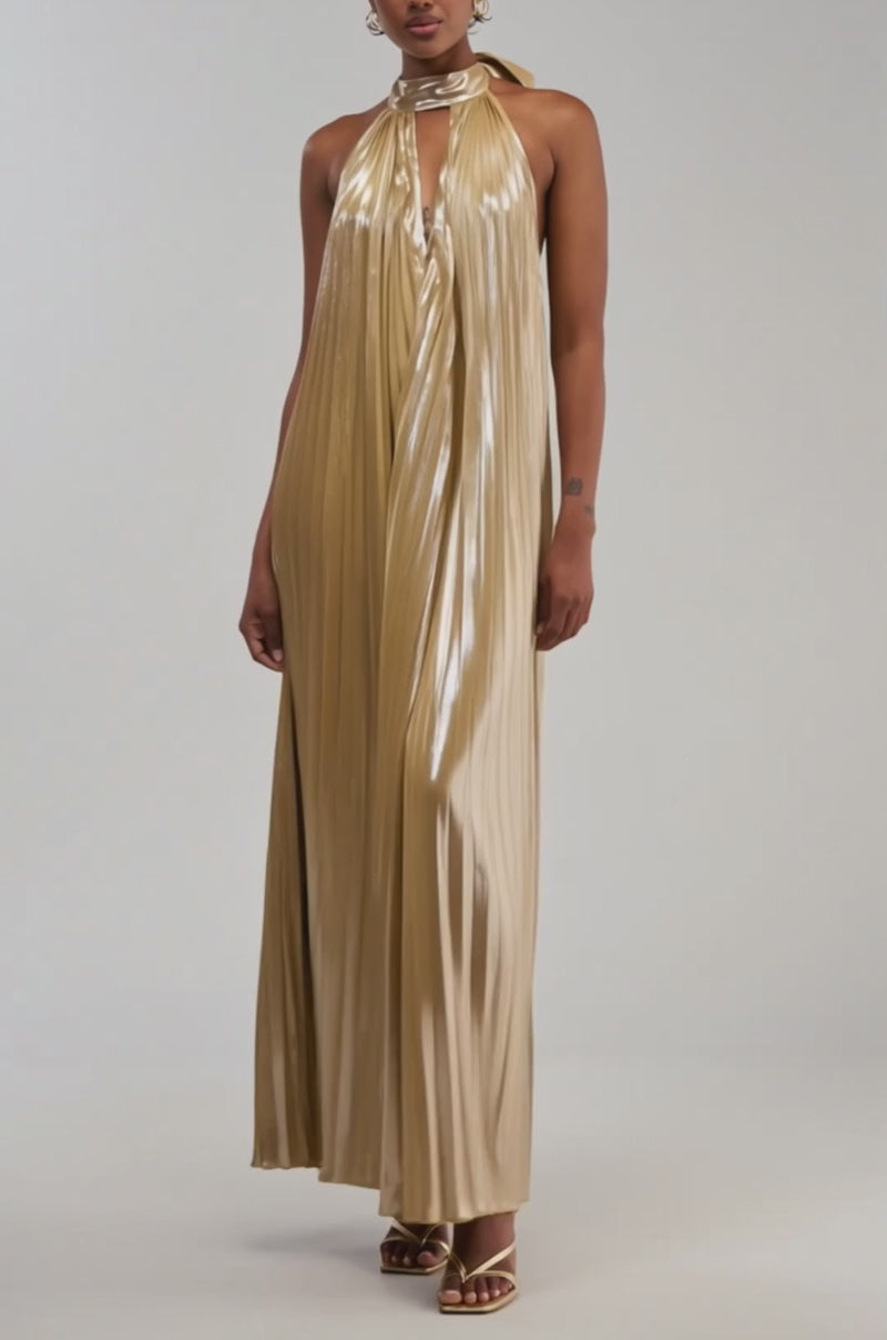 Video of a woman modeling the DRIPPING IN GOLD SATIN MAXI DRESS, featuring a shiny gold hue, elegant pleats, and a halter-neck with a keyhole neckline as she slightly holds out the skirt. 
