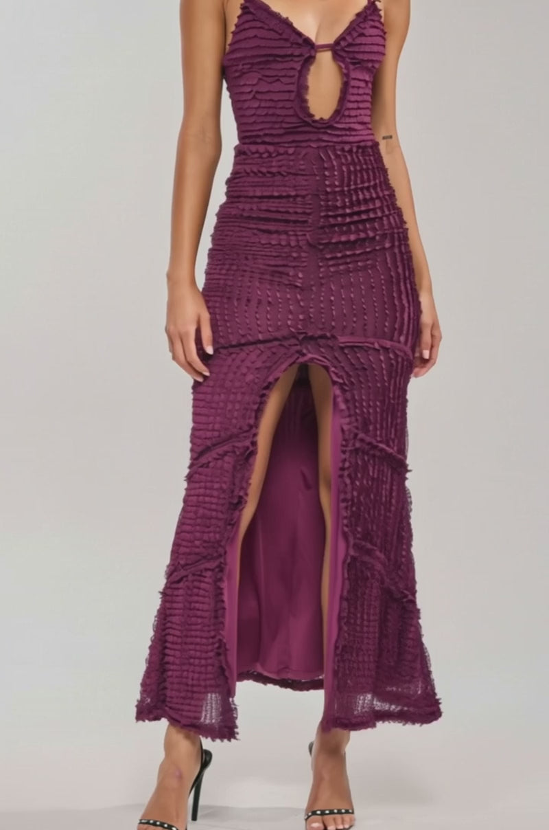 Video of woman modeling the PLUS ONE MAXI DRESS IN PLUM, a sleeveless cocktail dress featuring a plunging keyhole neckline, textured details, a front slit, and high-heeled sandals.