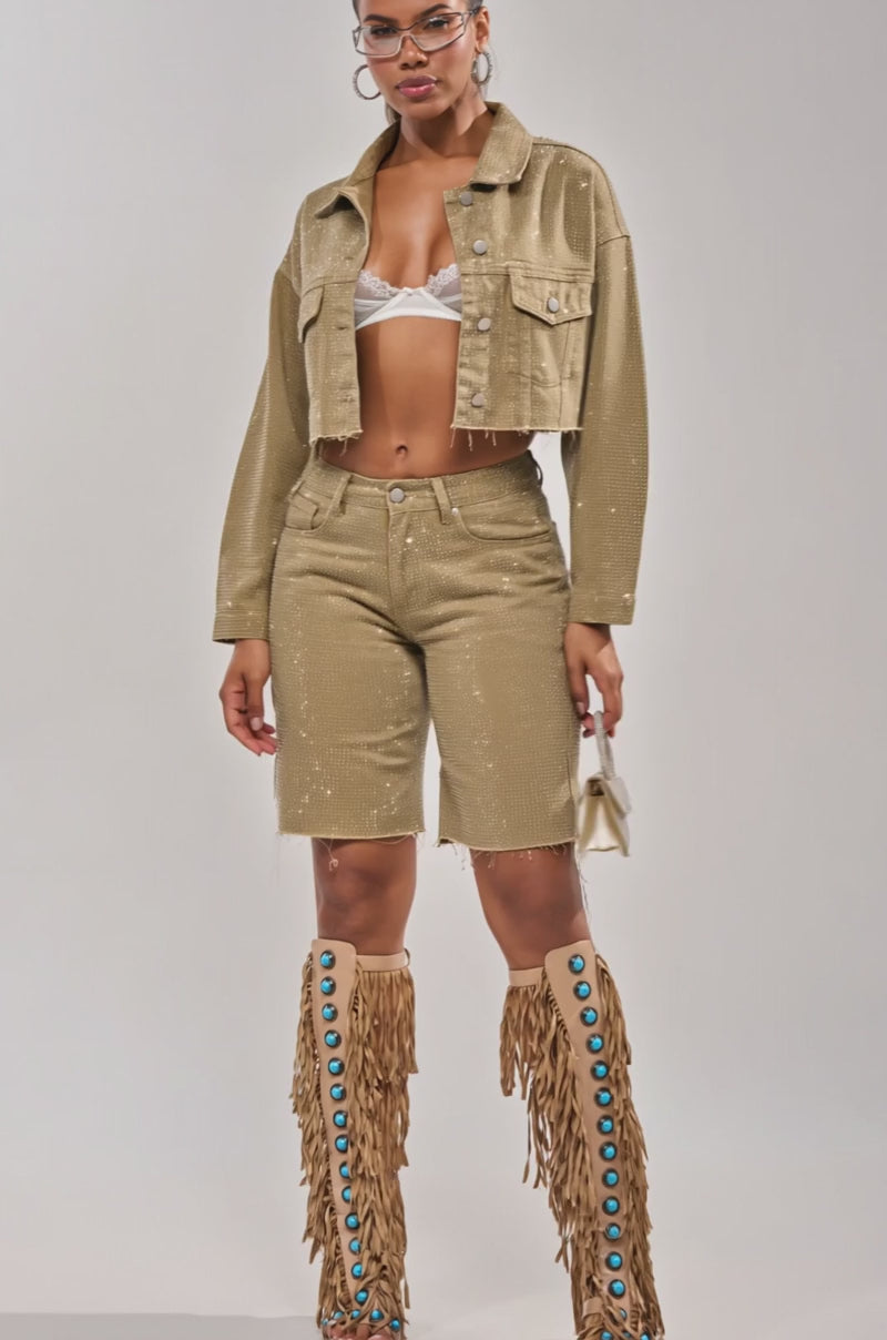 Video of woman modeling the CHECK OUT THE BLING BERMUDA SHORT in gold with rhinestones, a matching long-sleeve top, tan fringe boots with turquoise buttons, and holding a small sparkly silver handbag.
