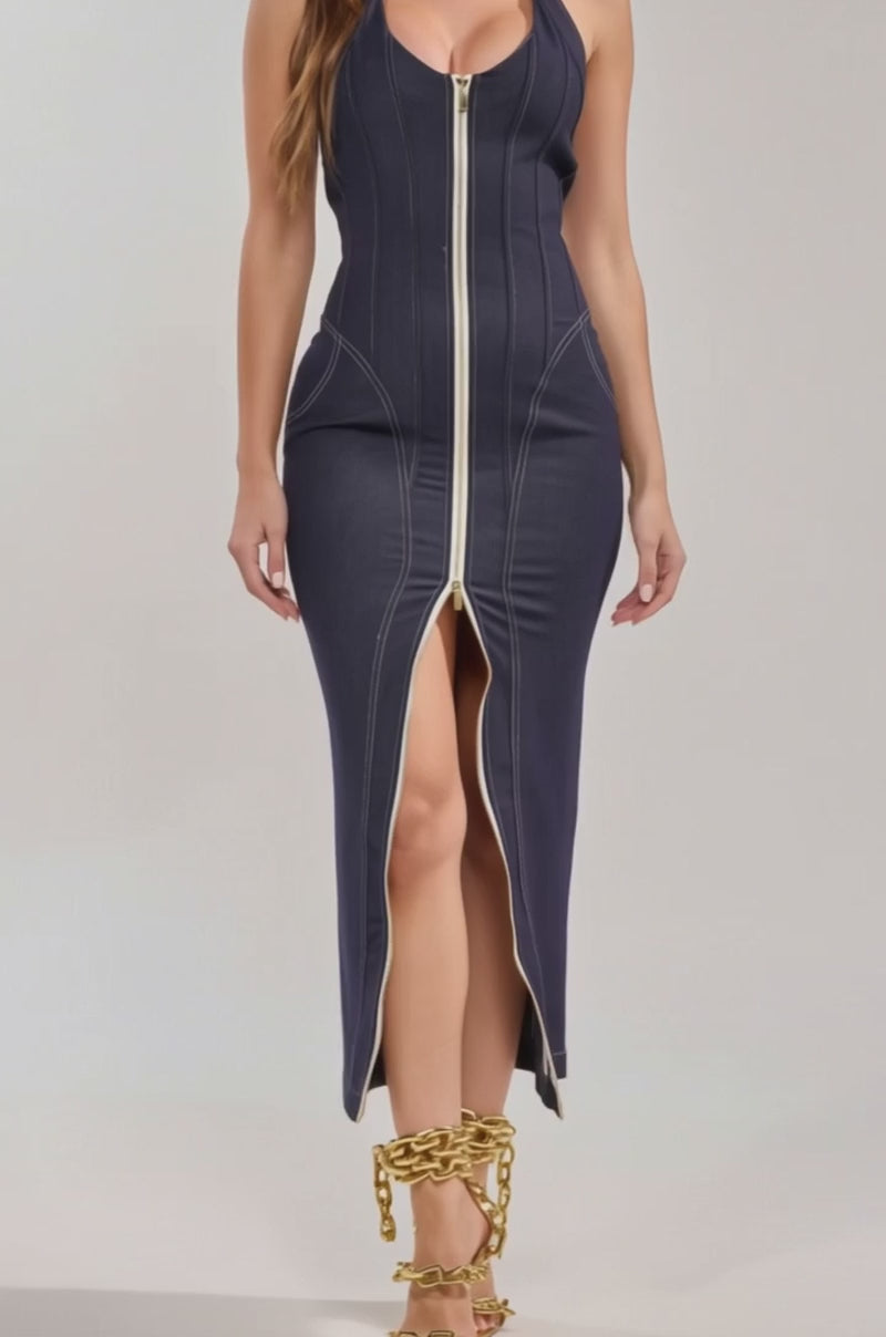 Video of woman modeling the JADA ZIP UP DENIM MAXI DRESS, a dark wash halter bodycon maxi with a front zipper from neckline to slit, styled with gold chain strappy high-heeled sandals against a plain background.