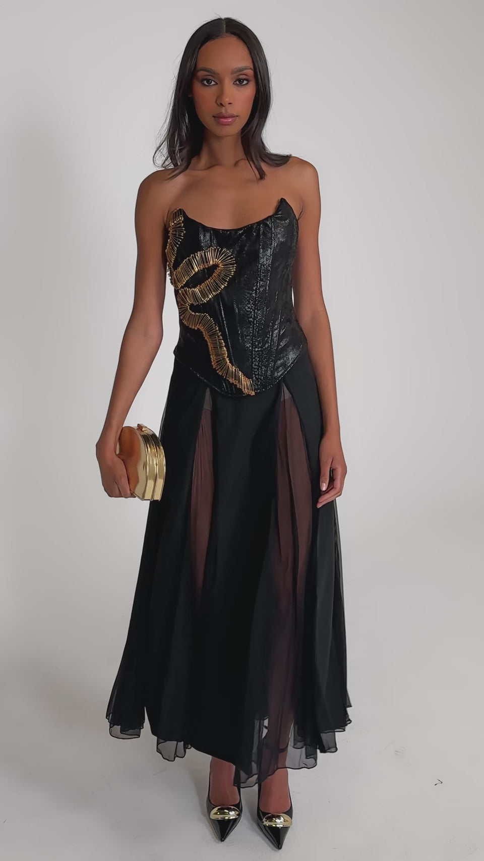 Video of woman modeling the SEXY MESH SKIRT, a matching crop top, black high heels with gold tips, and holding a small gold clutch.