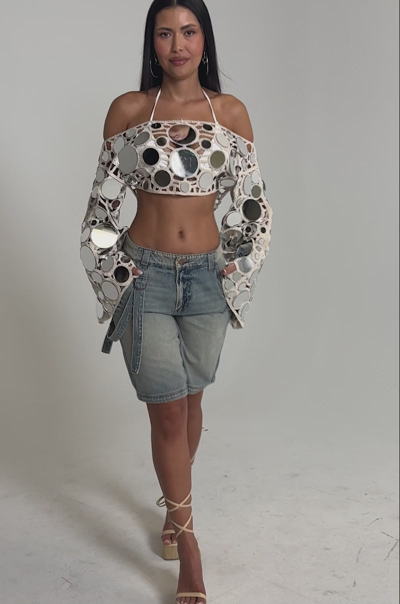 Video of woman modeling the RESORT VIBES CROCHET CROP LONG SLEEVE over a white halter, styled with loose-fitting blue jeans and a belt.