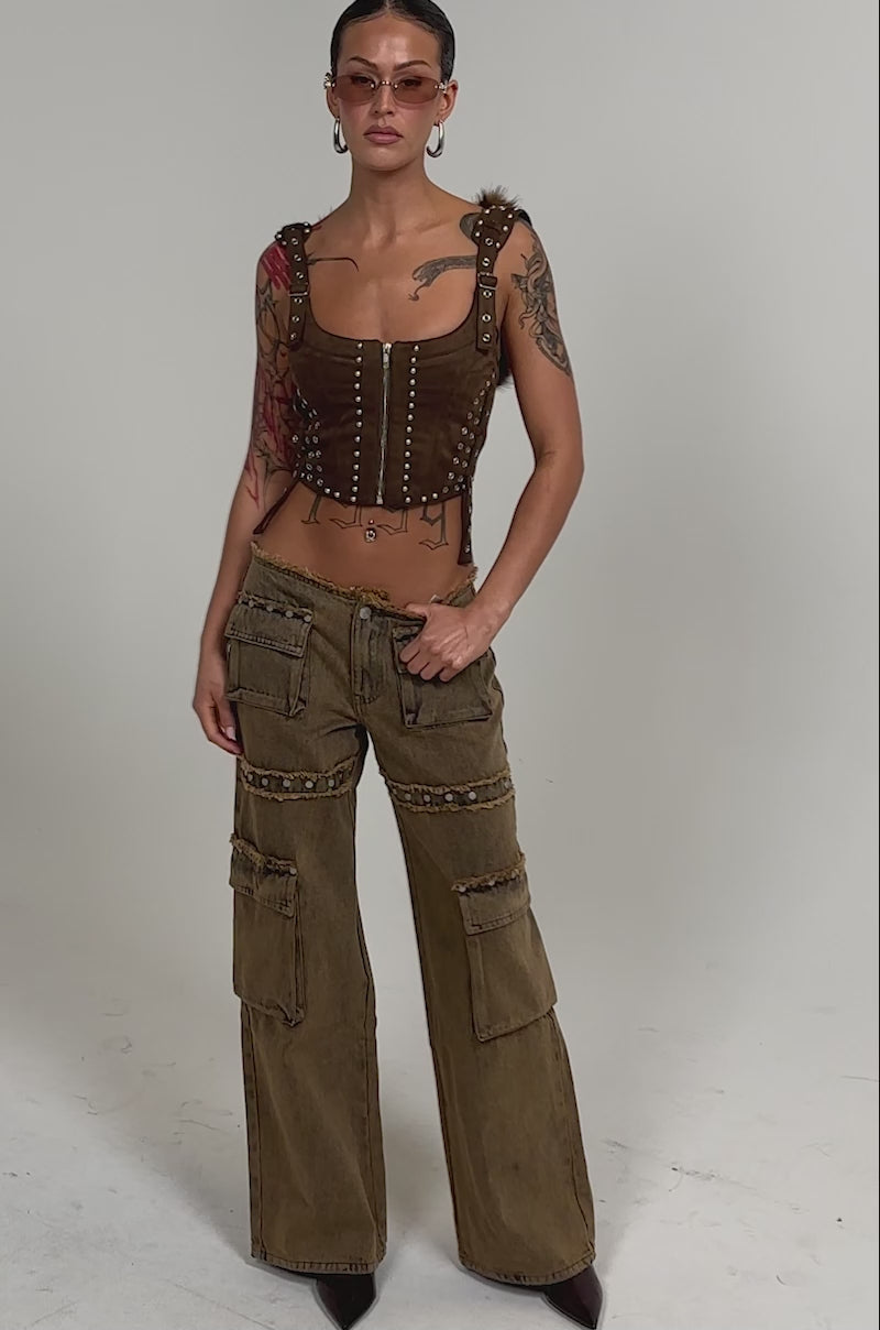 Video of woman modeling the OUT THE MUD DENIM JEANS with cargo pockets and chain details, a brown corset-style top, sunglasses, and heels.