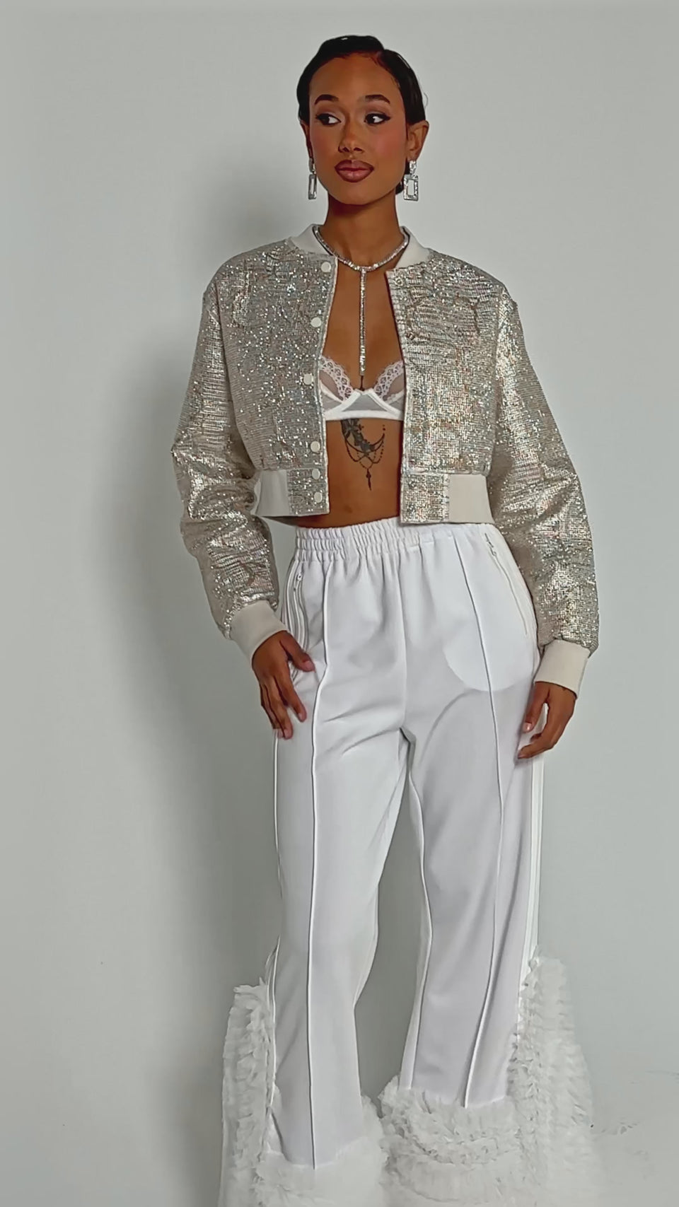 Video of woman modeling the GOLDEN HOUR EMBELLISHED BROCADE BOMBER over a white lace bralette and high-waisted white pants, styled with geometric earrings and a statement necklace.