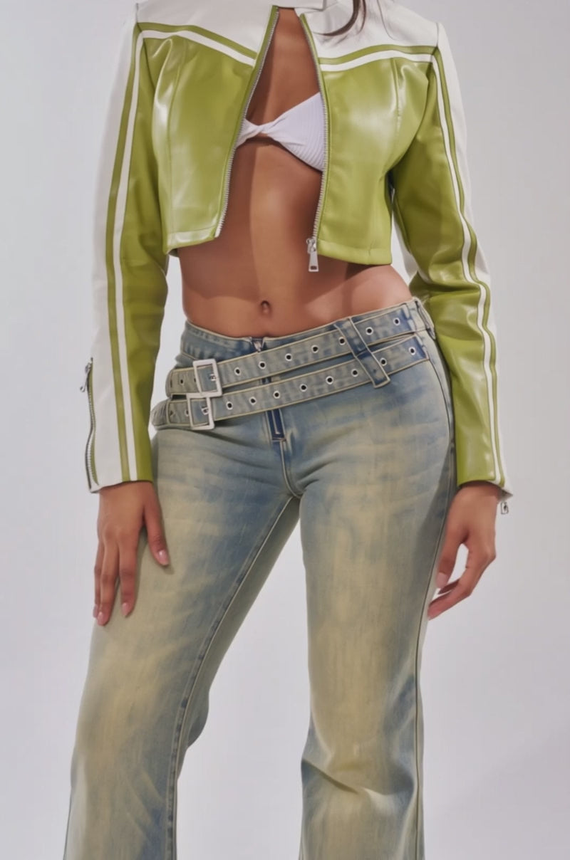 A video of a woman wearing the WEST LOOP RACER MOTO IN GREEN over a white bralette, light blue double-belted jeans, and tinted sunglasses.