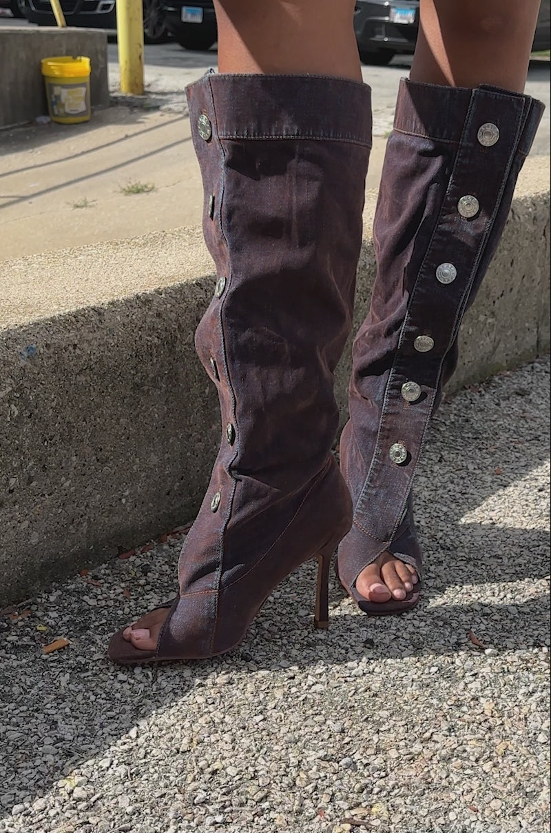 Video of person modeling the AZALEA WANG KAZUKI BURNT ORANGE SLOUCHY DENIM BOOT. It features a knee-high length in burnt orange denim with a stiletto heel, peep toe, and silver button details near the top and front opening.