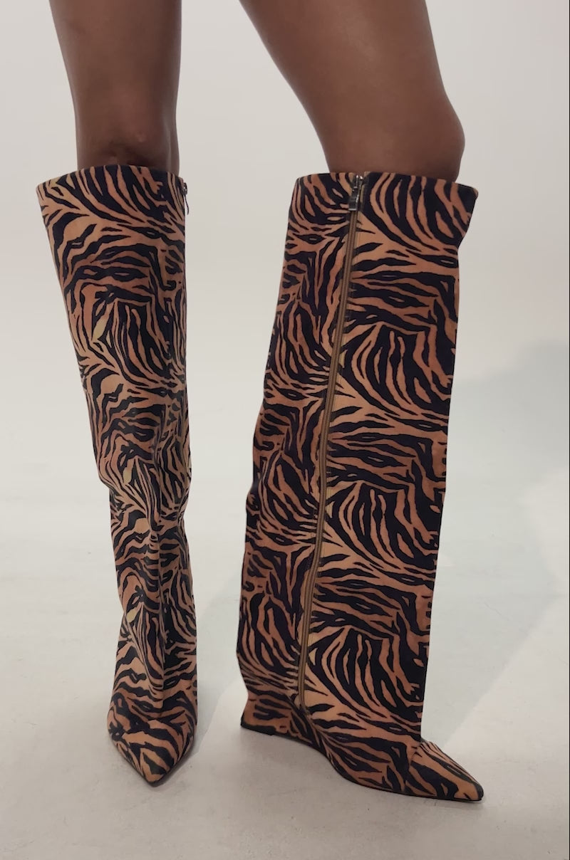 Video of woman modeling the AZALEA WANG KENYA TIGER WEDGE BOOT with bold orange and black stripes, paired with a black sparkly mini skirt, creating standout festival style that pops against a plain, light-colored background.