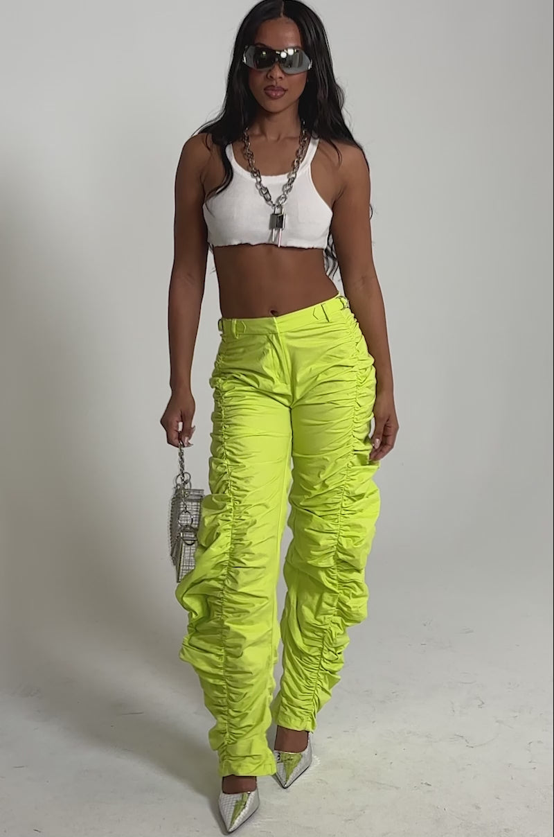 Video of woman modeling the NOT IN THE MOOD RUCHED TROUSER—bold, high-waisted statement pants. She accessorizes with a small silver geometric handbag and layered necklaces.