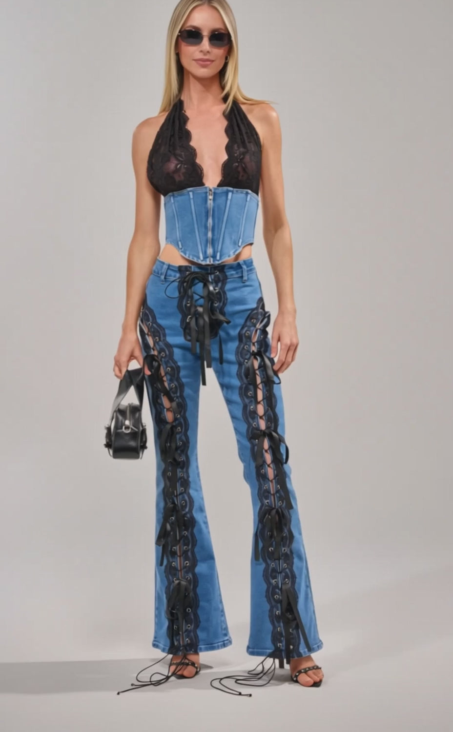 Video of woman modeling the LACED UP DENIM CORSET, paired with denim pants featuring lace-up thigh cutouts and a black lace halter top, standing against a neutral background.
