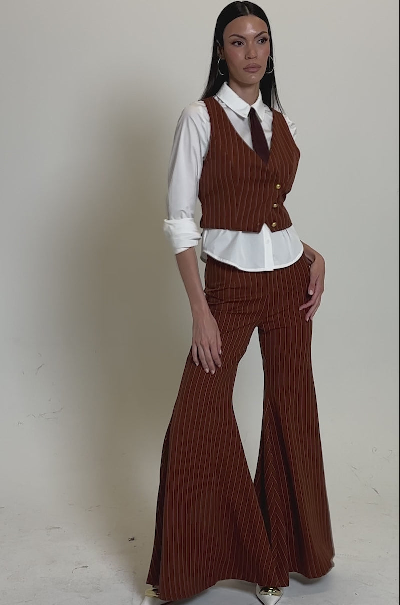 A video of a woman in the BUSINESS FIRST VEST—brown, pinstriped, and cropped—paired with flared pants, a white button-up shirt, and a maroon necktie.