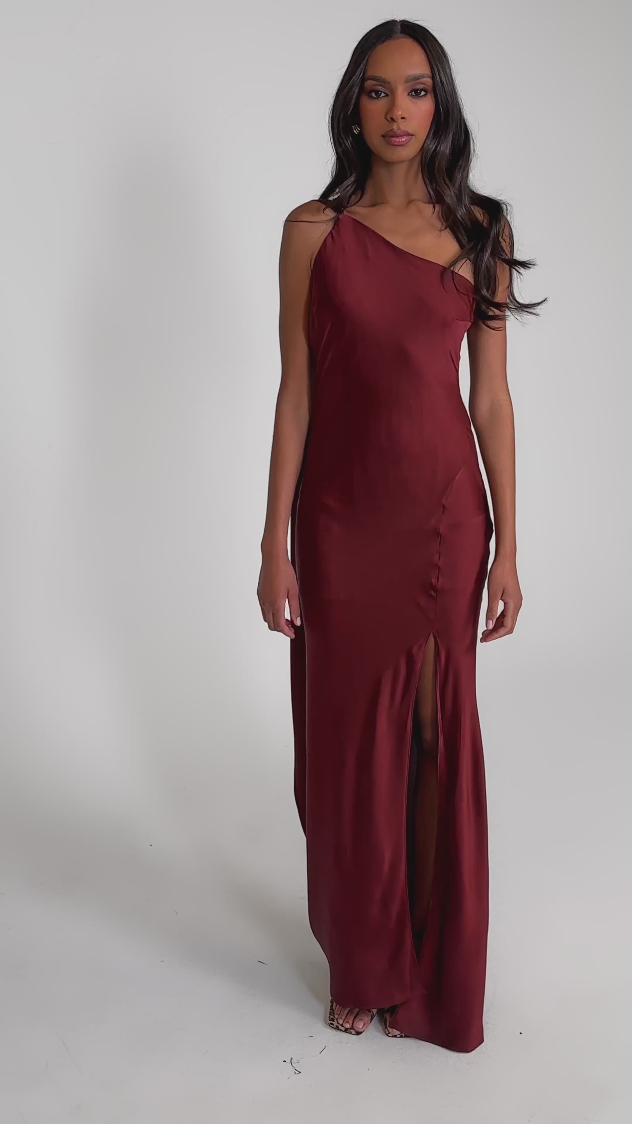 Video of woman modeling the RSVP READY SATIN MAXI DRESS, a wine-colored satin maxi with a side slit and matching scarf, stands against a plain light gray background.