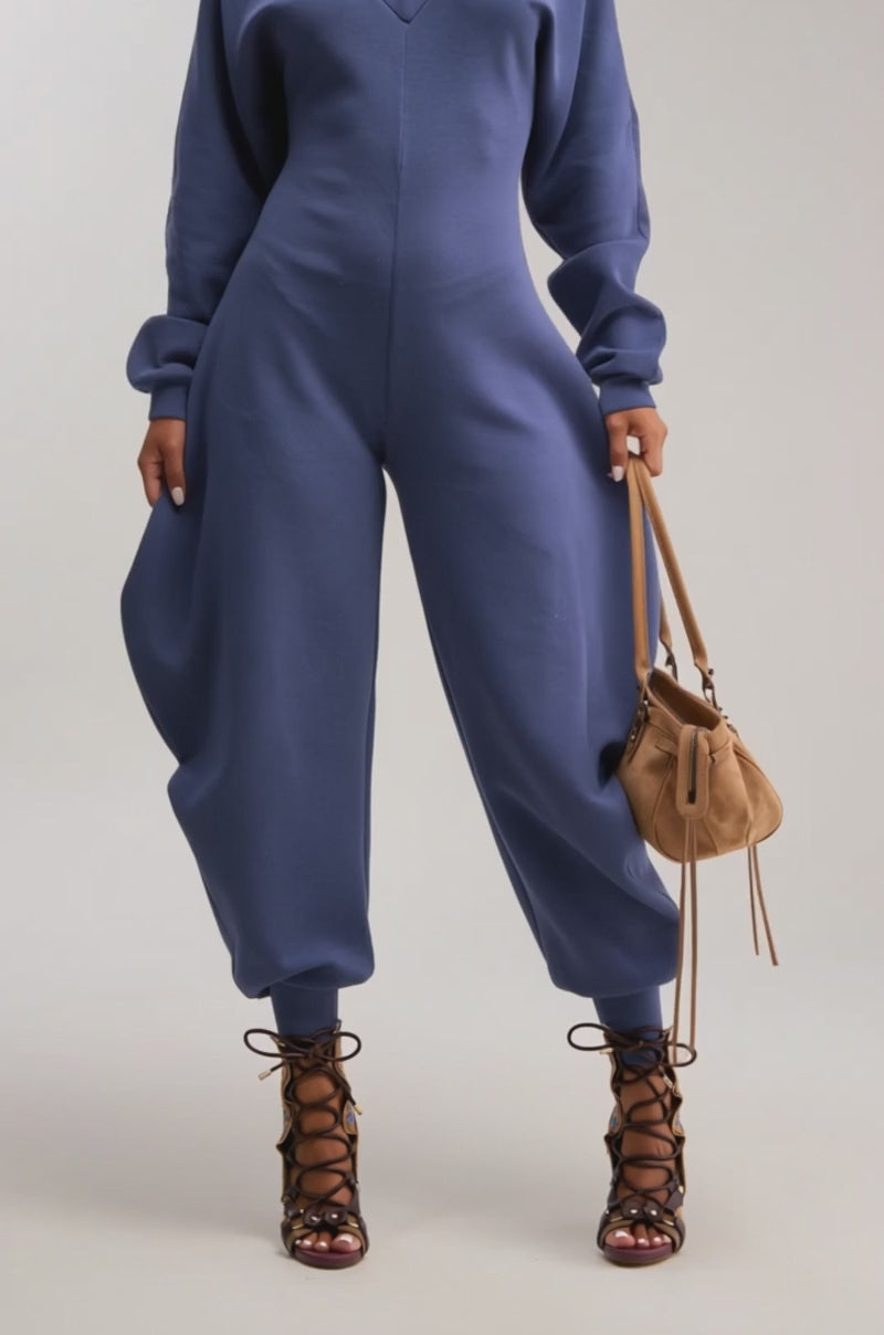 Video of woman modeling the COMFY COZY JUMPSUIT IN NAVY, featuring wide legs and fitted cuffs. She styles it with brown lace-up heels, sunglasses, and a tan handbag.