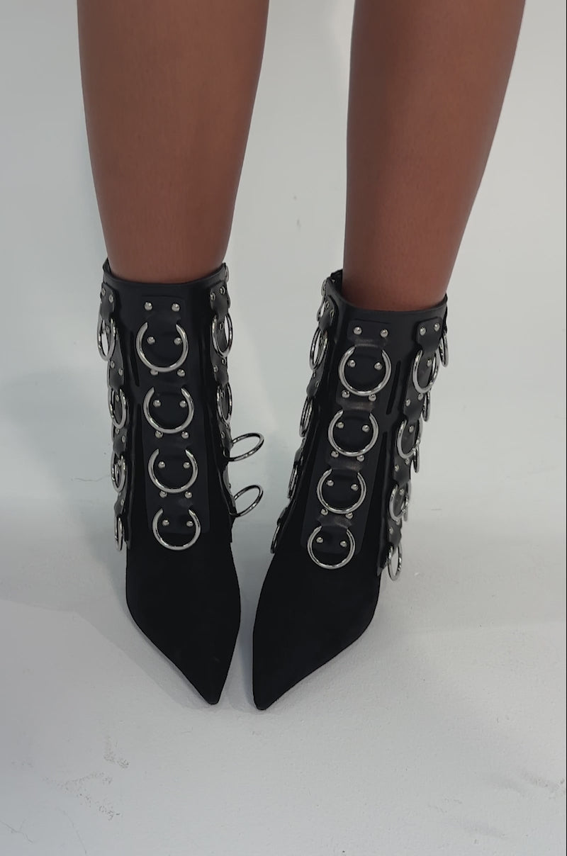 Video of woman modeling the AKIRA GOLD GERANIUM BLACK PIERCING STILETO BOOTIE, featuring multiple silver rings and hardware