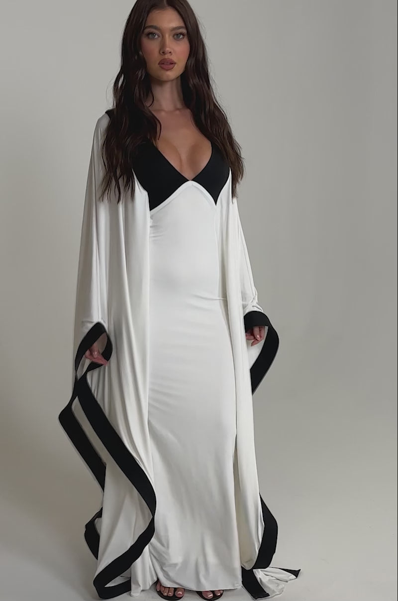 A video of a woman in the GUEST OF HONOR BODYCON MAXI DRESS, featuring a monochrome design with black accents on the neckline and hem. 
