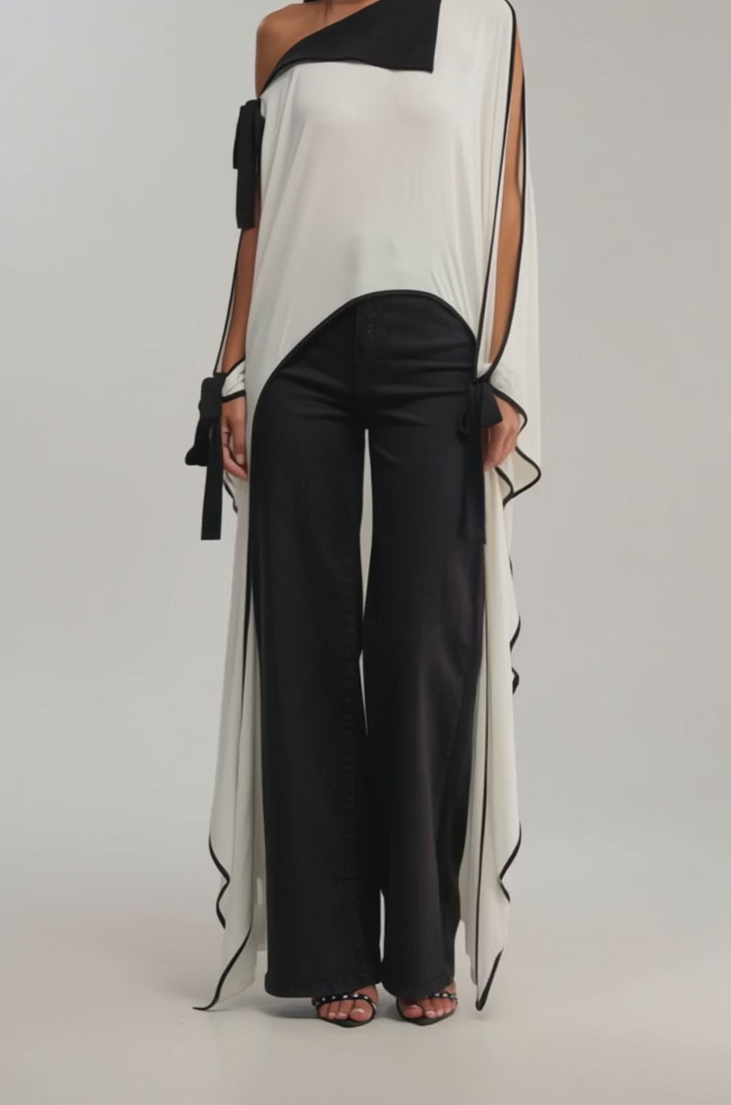 A video of a woman wearing the EMMA OFF THE SHOULDER CAPE with black trim and wide-legged black pants. 