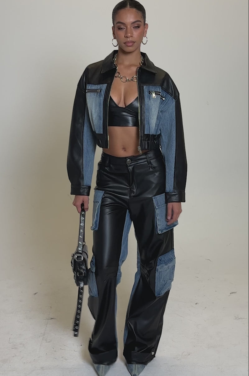 A video of a woman in the DOWN TIME MIXED MEDIA BOMBER, styled with a black bralette and high-waisted denim and black leather patchwork pants, pointed-toe shoes, and a chunky necklace.