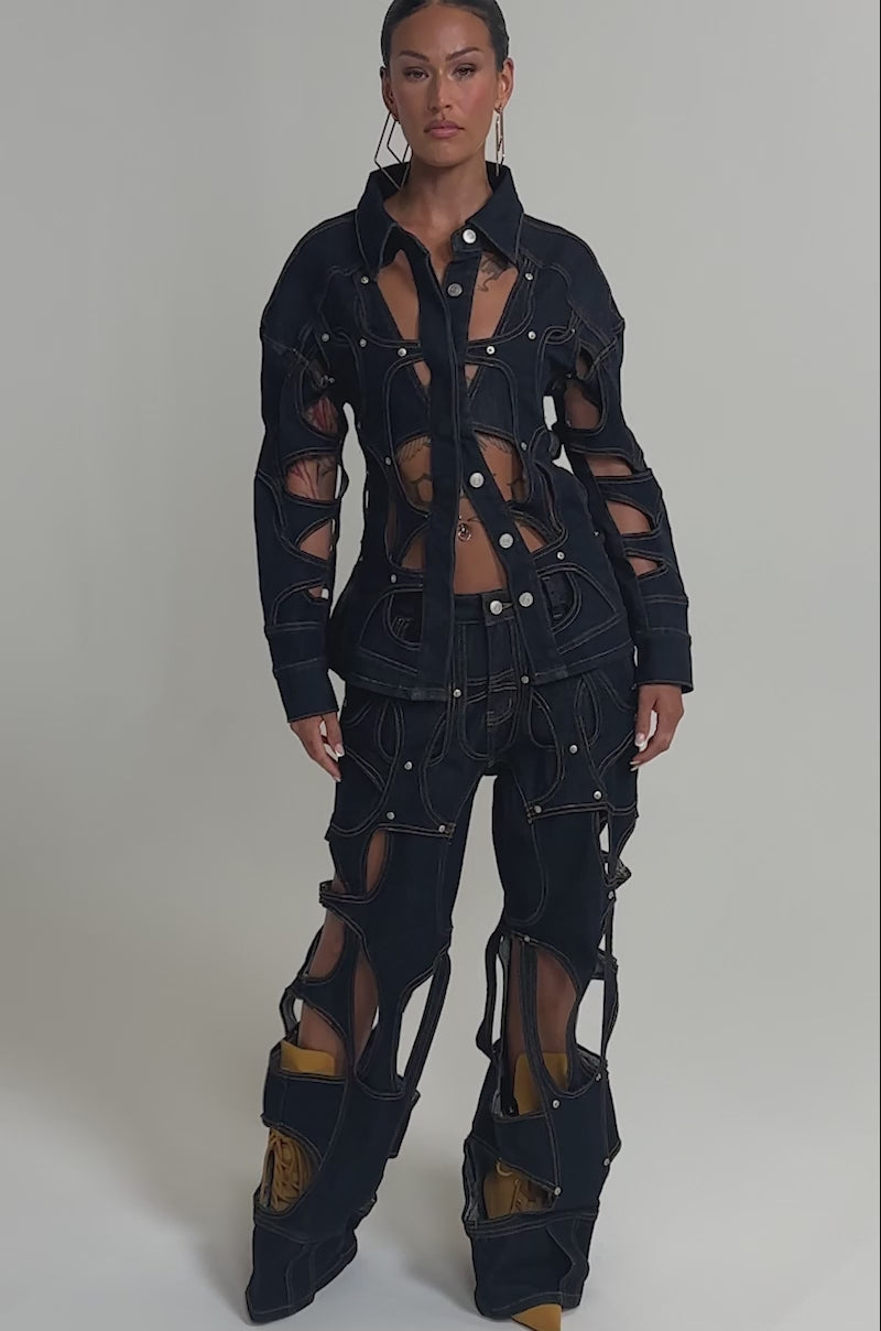 Video of woman modeling the CUT YOU OUT RELAXED DENIM—unique, deconstructed jeans with large cutouts and visible brown stitching that reveal skin and show yellow shoes through the open ankle sections.