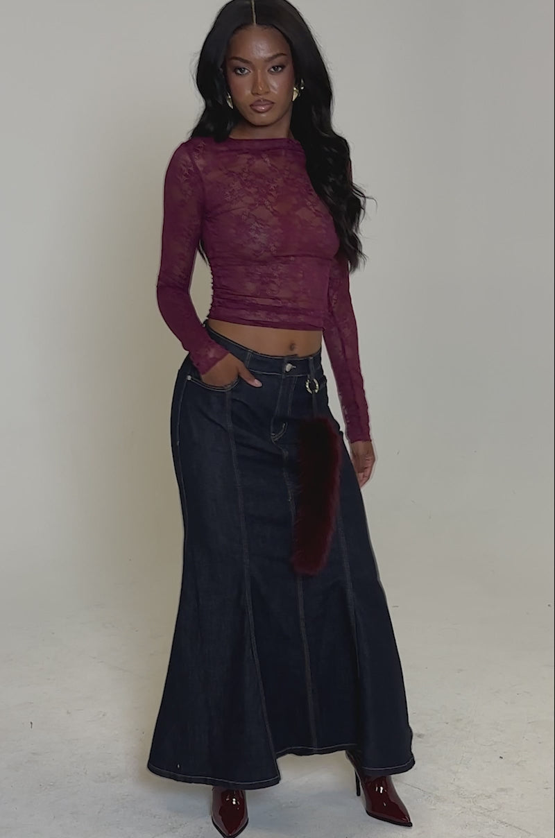 A video of a woman in the ESSENTIAL LACE LONG SLEEVE TOP IN PLUM, paired with a dark denim maxi skirt and burgundy boots. 