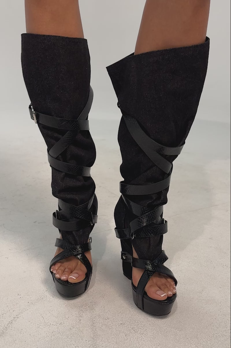 A video of the AZALEA WANG ROTHKID Black Denim Knee High Open Toe Boot which features a black wedge heel, multiple crisscrossing straps, and a textured finish.