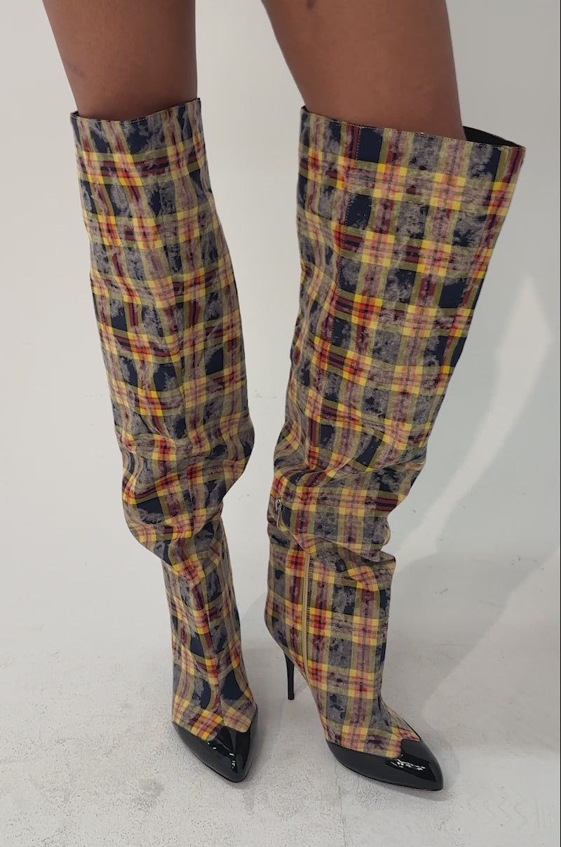 A video of a person in the AKIRA GOLD LOCHANA MULTI YELLOW PLAID FLANNEL SEXY BOOT, featuring a pointed toe, yellow plaid pattern with red and blue checks, and sleek black tips.