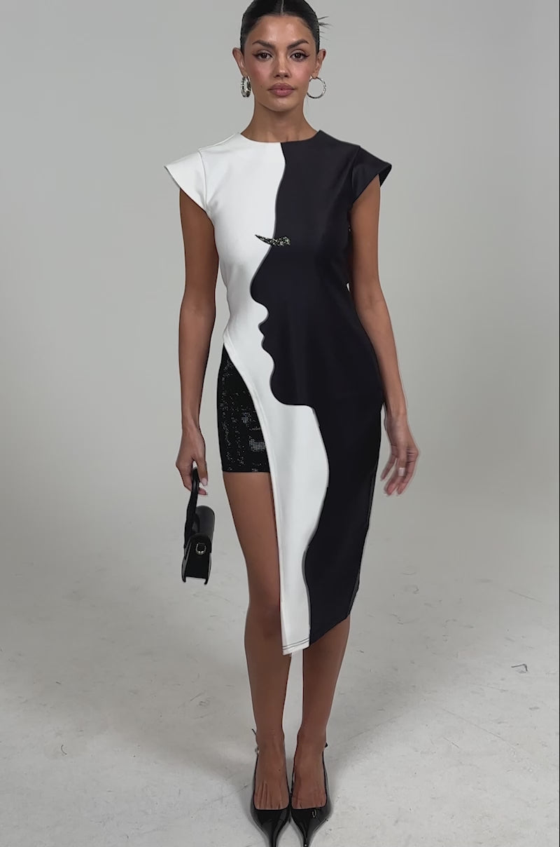 Video of woman SILHOUETTE LONGLINE TEE, a sleeveless two-tone top with bold black-and-white face profiles along the color divide. She carries a small black handbag and her hair is styled in a sleek bun.
