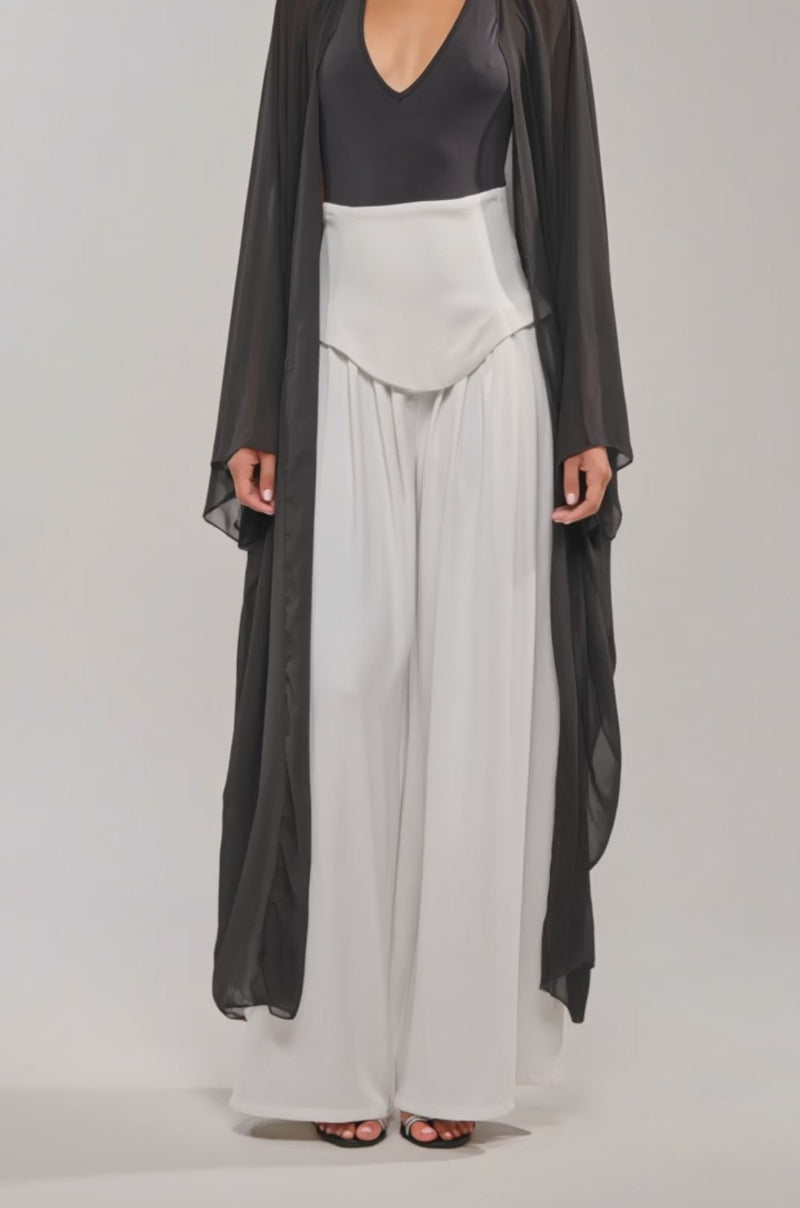 Video of woman modeling the ADDAMS CAPE BODYSUIT, styled with wide-leg white pants, creating a striking editorial look against a plain light background.