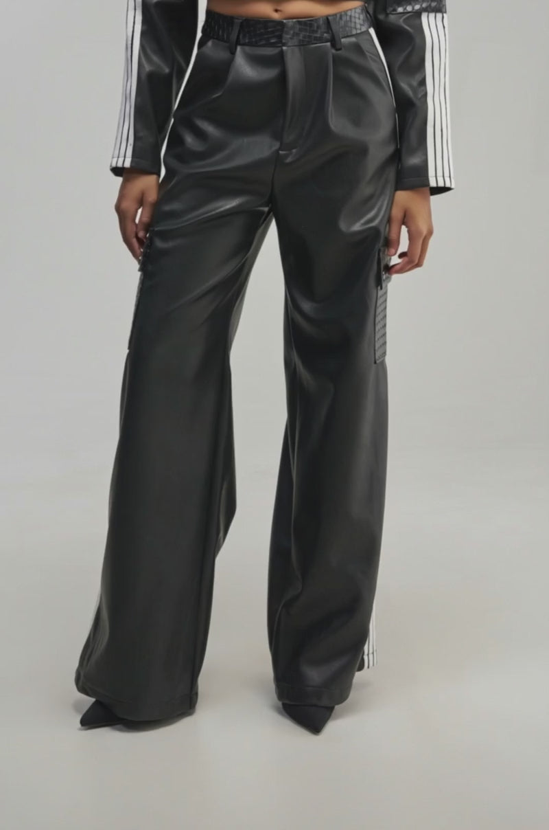 Video of a woman modeling the DONT TEST ME FAUX LEATHER TROUSER in black, styled with a matching black top featuring bold white racing stripes on the sleeves, standing against a plain background.