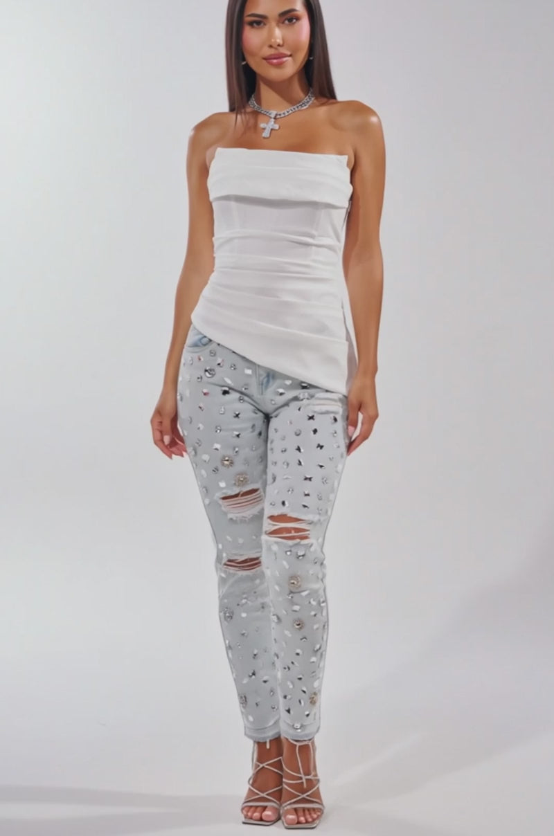 A video of a woman in the PRETTY PRINCESS CORSET IN WHITE, paired with light blue ripped gem-embellished jeans, strappy silver heels, and layered necklaces.
