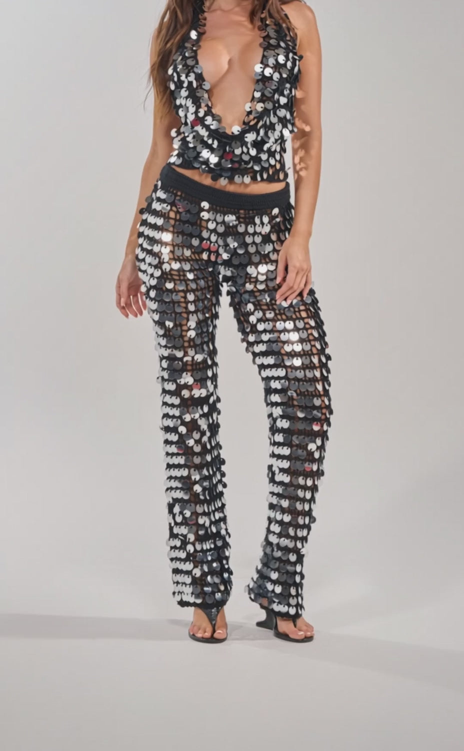 A video of a woman wearing the GIVE IT TO ME BABY CROCHET BRALETTE and matching sequin pants, styled with black high-heeled sandals.