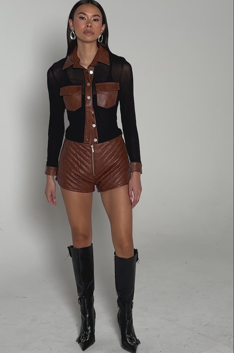 Video of woman modeling the GALAXY MESH BUTTON DOWN WITH FAUX LEATHER TRIM and brown quilted leather shorts, standing against a plain light background.