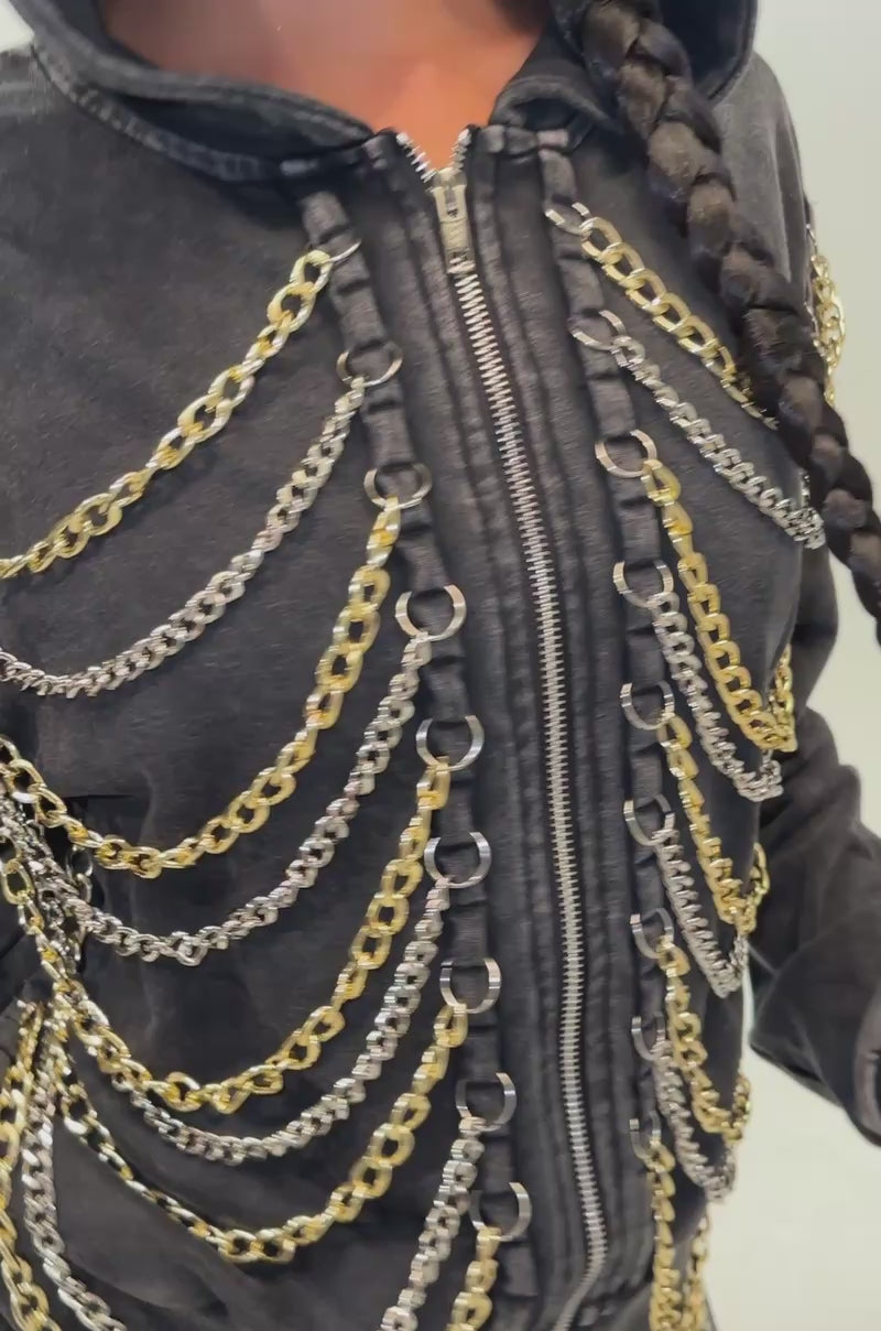 Video of a woman modeling the CHAINED DOWN SWEATSHIRT in washed black, featuring statement chain detailing. She completes her bold streetwear look with multiple gold chains, large hoop earrings, and a long braided hairstyle while standing against a plain background.