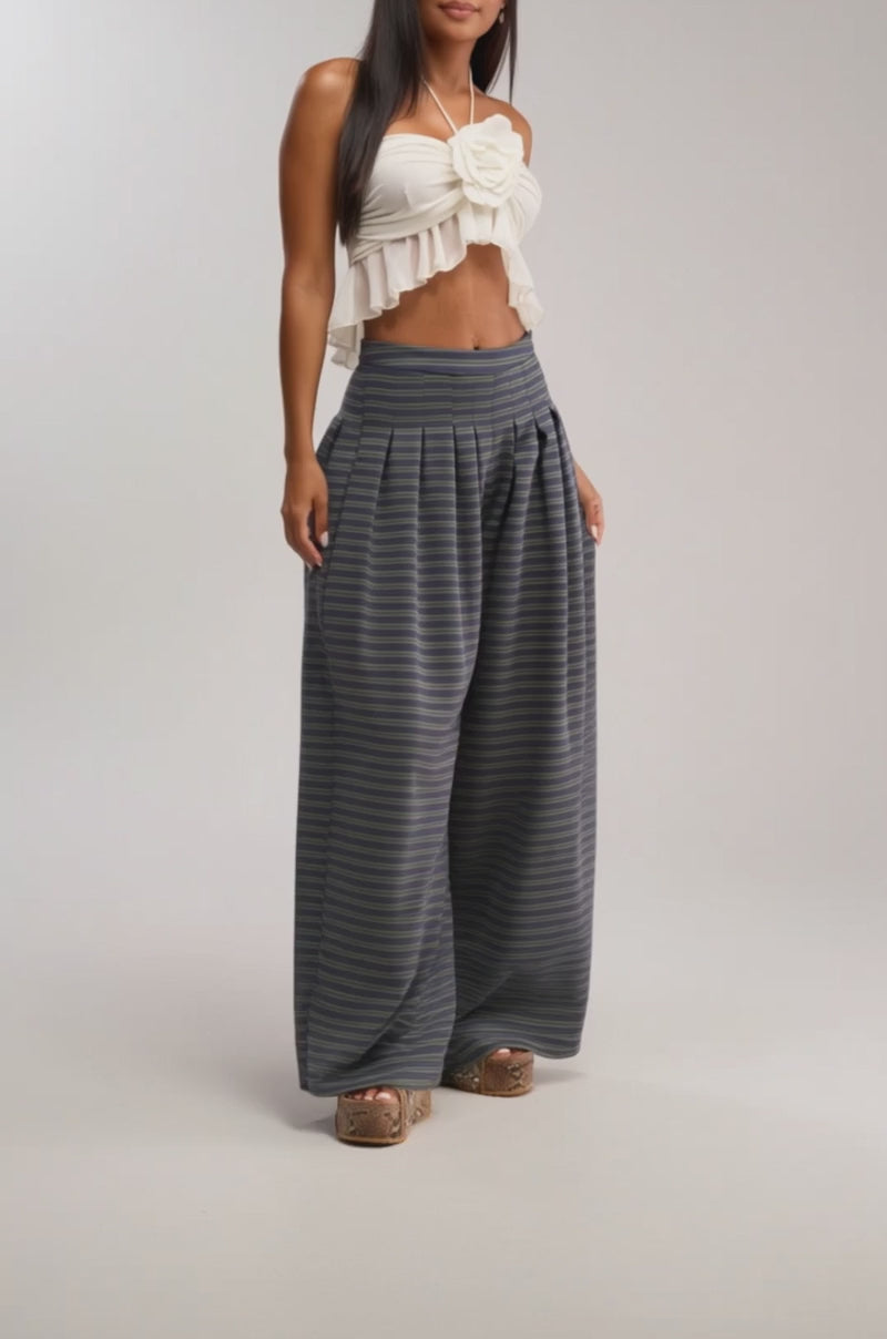 A video of a woman in the GUESS WHO STRIPE PALAZZO PANT and a white ruffled crop top, paired with patterned platform shoes against a plain background.