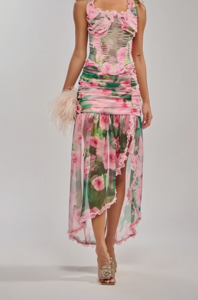 Video of woman modeling the DREAMING FLORAL MAXI SKIRT, a sheer pastel high-low skirt with lace trim and high-rise fit, paired with a feathery clutch and gold embellished heels, shown from shoulders down.