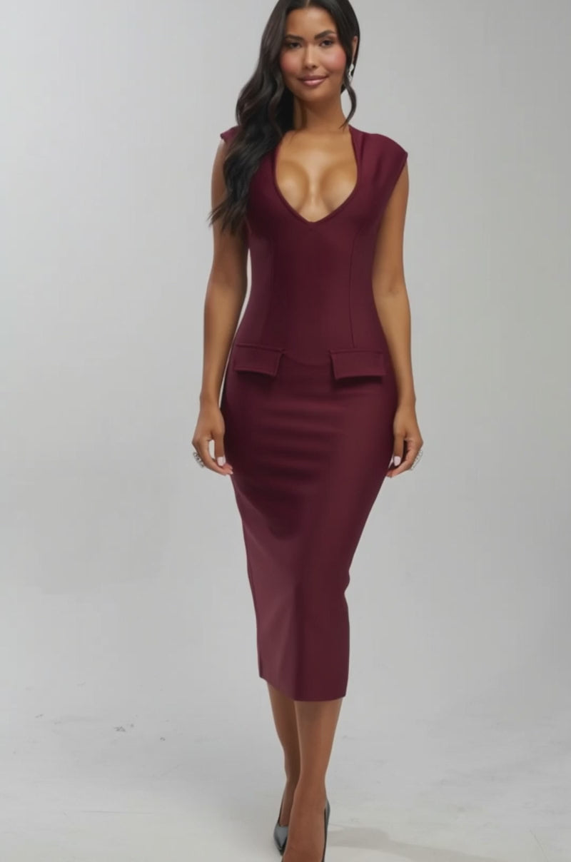 Video of woman modeling the KISS & TELL BANDAGE MIDI DRESS, a fitted sleeveless burgundy midi with a deep V-neckline and two decorative waist flaps, standing before a plain light gray background.