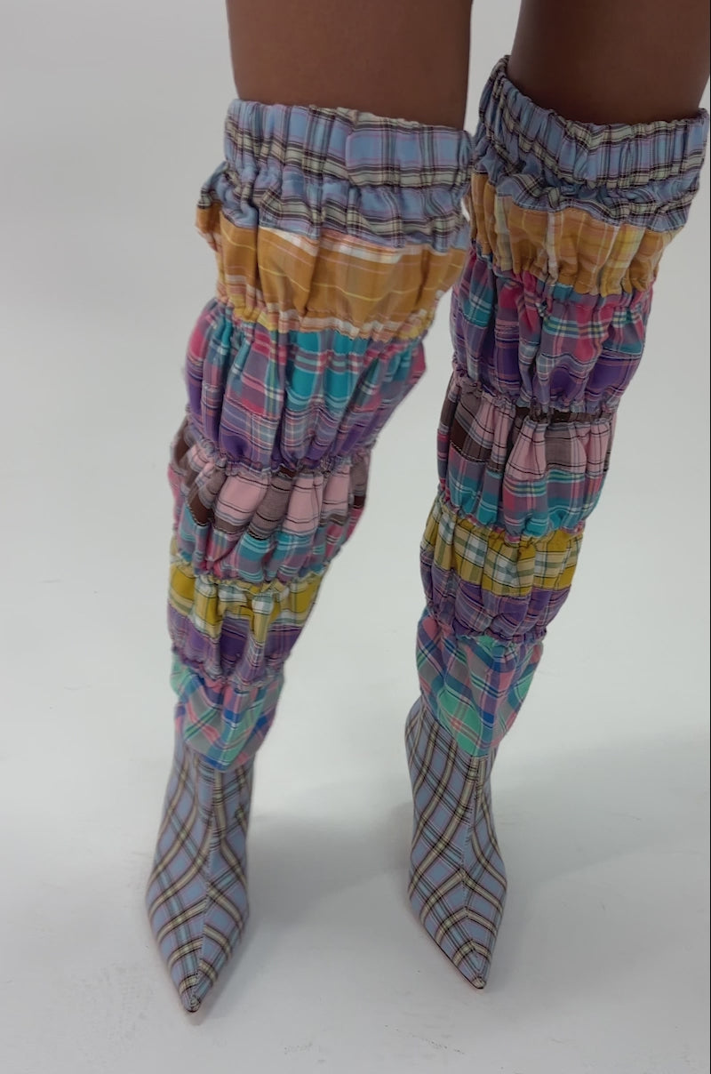 Video of woman modeling the AZALEA WANG ELODIE PINK MULTI BOXER BOOT—thigh-high stiletto boots in pastel pink, purple, yellow, and blue plaid with pointed toes—standing against a plain white background.