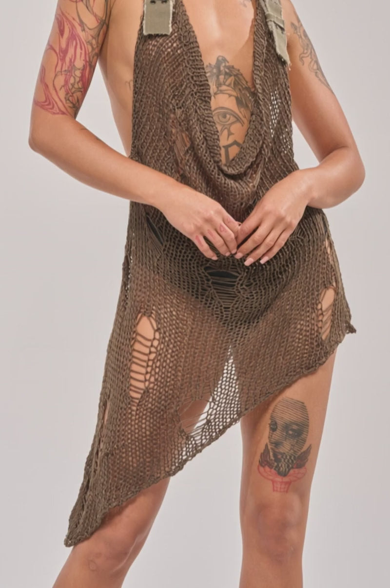 Video of woman modeling the MAKE A MESS KNIT MINI DRESS IN OLIVE, a sleeveless, asymmetrical mini dress with a low neckline and strap details, set against a plain light background.