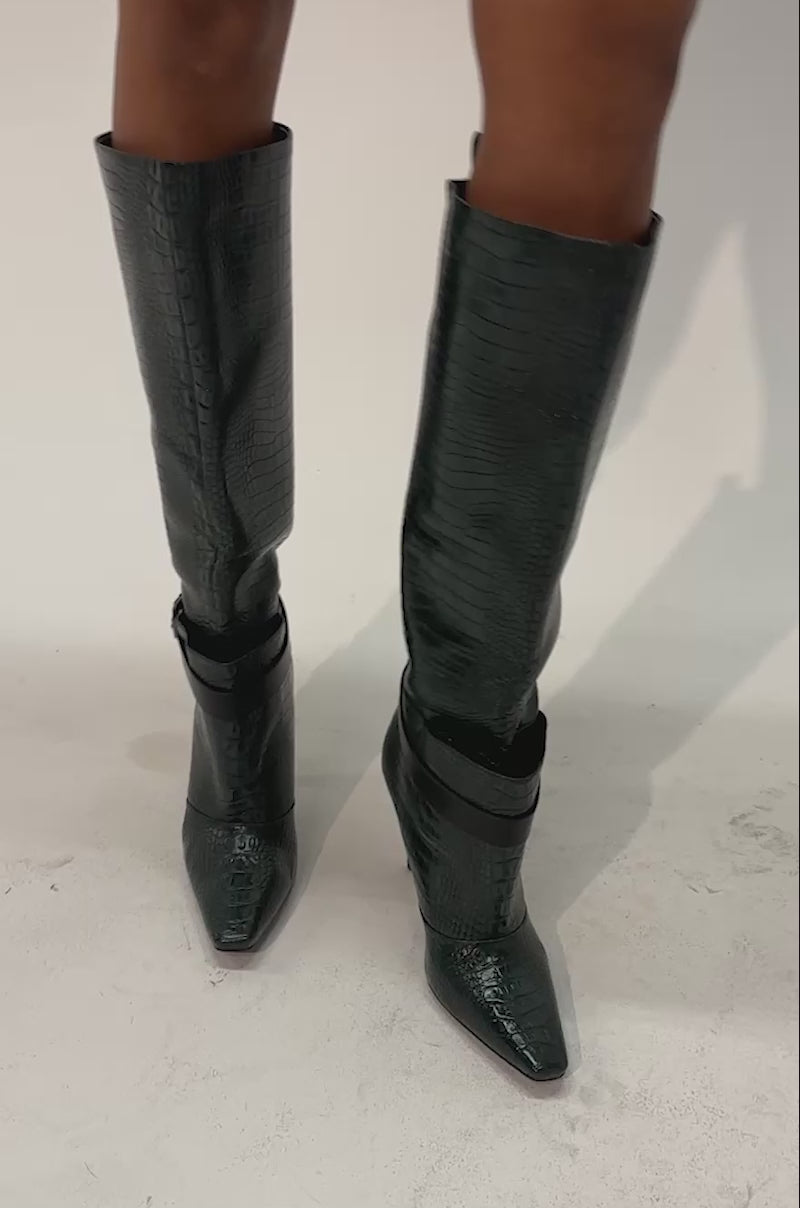 Video of a woman modeling the AZALEA WANG ARIELLE EMERALD GREEN CROC BOOT—a knee-high stiletto with a textured croc-embossed faux leather finish and black buckle straps.