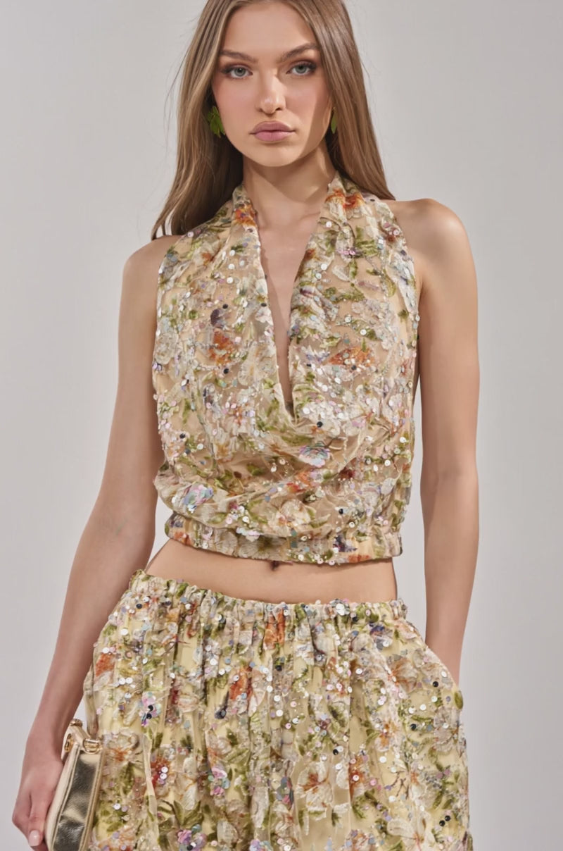 A video of a woman with long, straight hair poses confidently in the LETS TALK ABOUT IT COWL NECK top and matching skirt, holding a small gold clutch. 