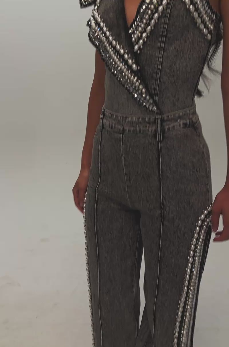 Video of a woman modeling the LUXURIOUS DENIM PANTS WITH SIDE SLITS IN GREY, featuring flared legs with subtle side slits, zigzag trim, and pearl rhinestone embellishments in a washed grey denim.
